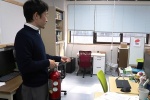 初期消火班として火元の研究室での消火活動訓練く説明する竹本教授