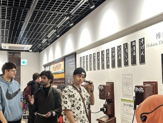 International students attentively listening to the Hakata dialect exhibit at the Hakata Machiya Furusato Museum.