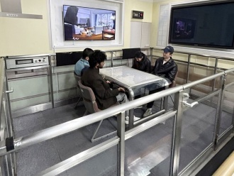 International students experiencing a simulated seismic intensity of 7, with the screen behind them showing large furniture falling during the earthquake scenario.